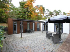Eine moderne Außenpatio mit Ziegelboden, einer überdachten Sitzgelegenheit und einem Gebäude aus Holz mit Glasfenstern.