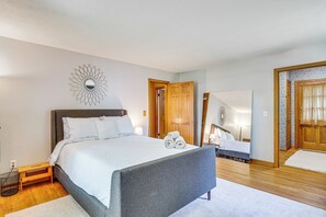 Ein Schlafzimmer mit einem großen Bett, einem Nachttisch, einem Spiegel und einer Tür zu einem anderen Raum.