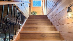 A wooden staircase with metal railings, a window at the top, and a light fixture on the right. - Mohawk Vista A-Frame Cabin (Blairsden-Greagle)