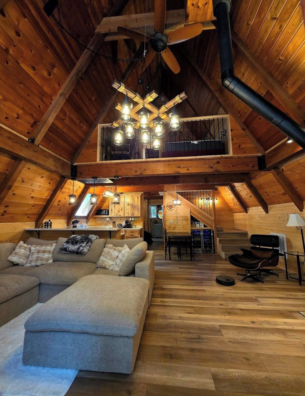 A spacious loft with a high ceiling, exposed wooden beams, a large sofa, a dining area, and a kitchen.