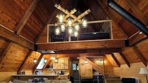 A spacious loft with a high ceiling, exposed wooden beams, a large sofa, a dining area, and a kitchen. - Mohawk Vista A-Frame Cabin (Blairsden-Greagle)