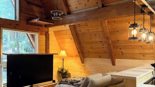 A cozy cabin interior with a wooden ceiling, a sofa, a TV, and a dining area. - Mohawk Vista A-Frame Cabin (Blairsden-Greagle)
