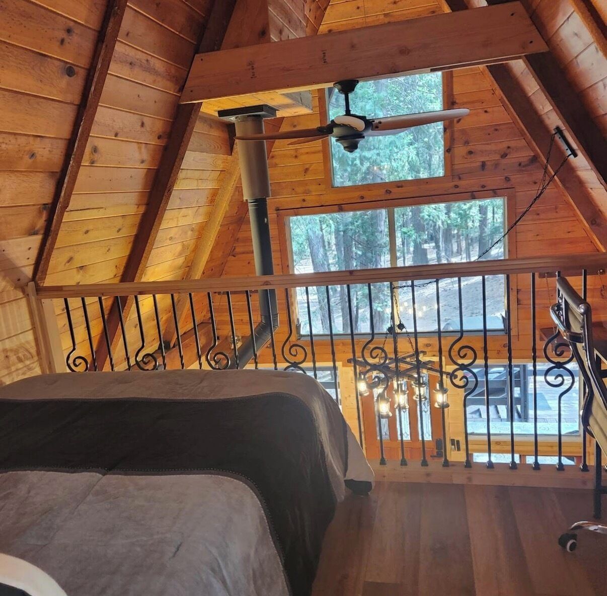 A wooden cabin with a loft bedroom, a ceiling fan, and a view of the forest.