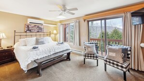 A bedroom with a bed, a bench, two armchairs, a ceiling fan, a large window, and a view of trees. - 2 Homes | Heated Pool + Game Room + Sauna | Mins to Gore Mountain (North Creek)