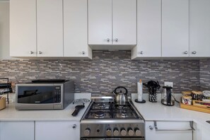 Une cuisine avec des meubles blancs, un four à micro-ondes, une cuisinière à gaz et un dosseret carrelé.