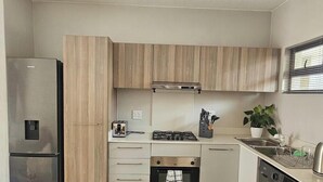 A compact kitchen with a stainless steel refrigerator, a gas stove, a built-in oven, and a dishwasher. - 1st Generation style (City of Johannesburg Metropolitan Municipality)