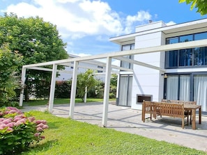 Ein modernes Haus mit überdachter Terrasse, einer Holzbank und einem Rasen.