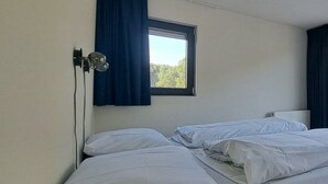 Ein Einzelbett mit weißer Bettwäsche in einem Zimmer mit Fenster und Wandlampe.