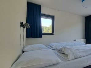 Ein Einzelbett mit weißer Bettwäsche in einem Zimmer mit Fenster und Wandlampe.