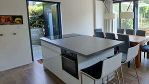 Eine moderne Küche mit einer zentralen Kochinsel, Essbereich mit Stühlen und großen Fenstern.