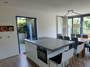 Eine moderne Küche mit einer zentralen Kochinsel, Essbereich mit Stühlen und großen Fenstern.