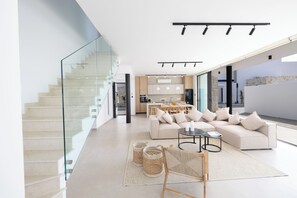A modern living room with a sofa, coffee table, and a staircase with glass railings. - New 4 Bedroom Villa With Pool, 100 Meters From the Beach (Paralimni)