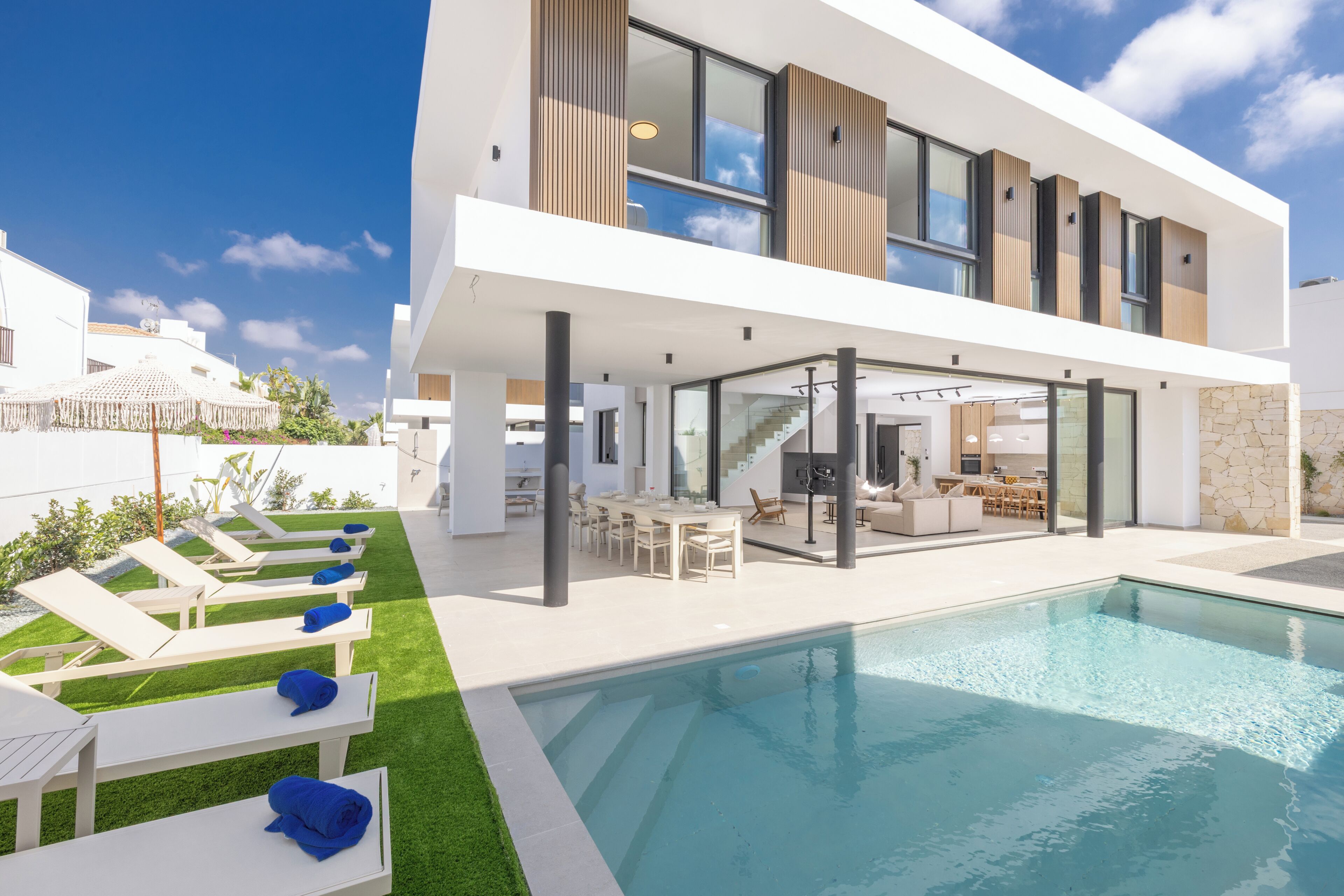 A modern two-story house with a swimming pool, outdoor seating, and a kitchen area.