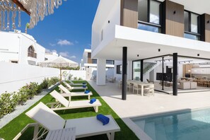 A modern outdoor pool area with lounge chairs, a dining area, and a staircase leading to an upper level. - New 4 Bedroom Villa With Pool, 100 Meters From the Beach (Paralimni)