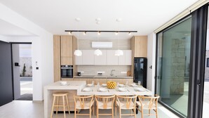 A modern kitchen with a central island, pendant lights, and a dining area with chairs and a table set for six. - New 4 Bedroom Villa With Pool, 100 Meters From the Beach (Paralimni)