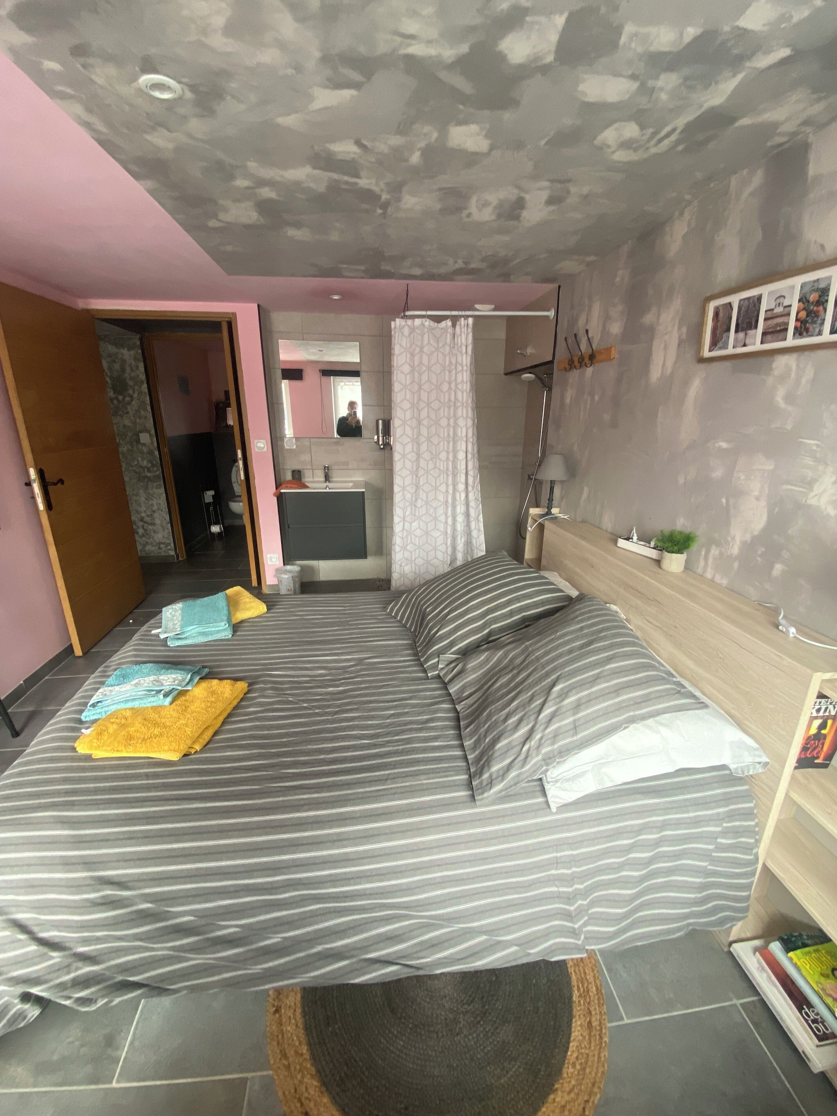 A bedroom with a bed, a bathroom, a wooden headboard, and a small shelf with books.