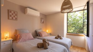 Un dormitorio con dos camas, una ventana con vistas a árboles, una lámpara colgante y un aire acondicionado de pared.