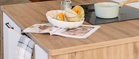 Una encimera de cocina con un bol de fruta, una tabla de cortar y una olla.