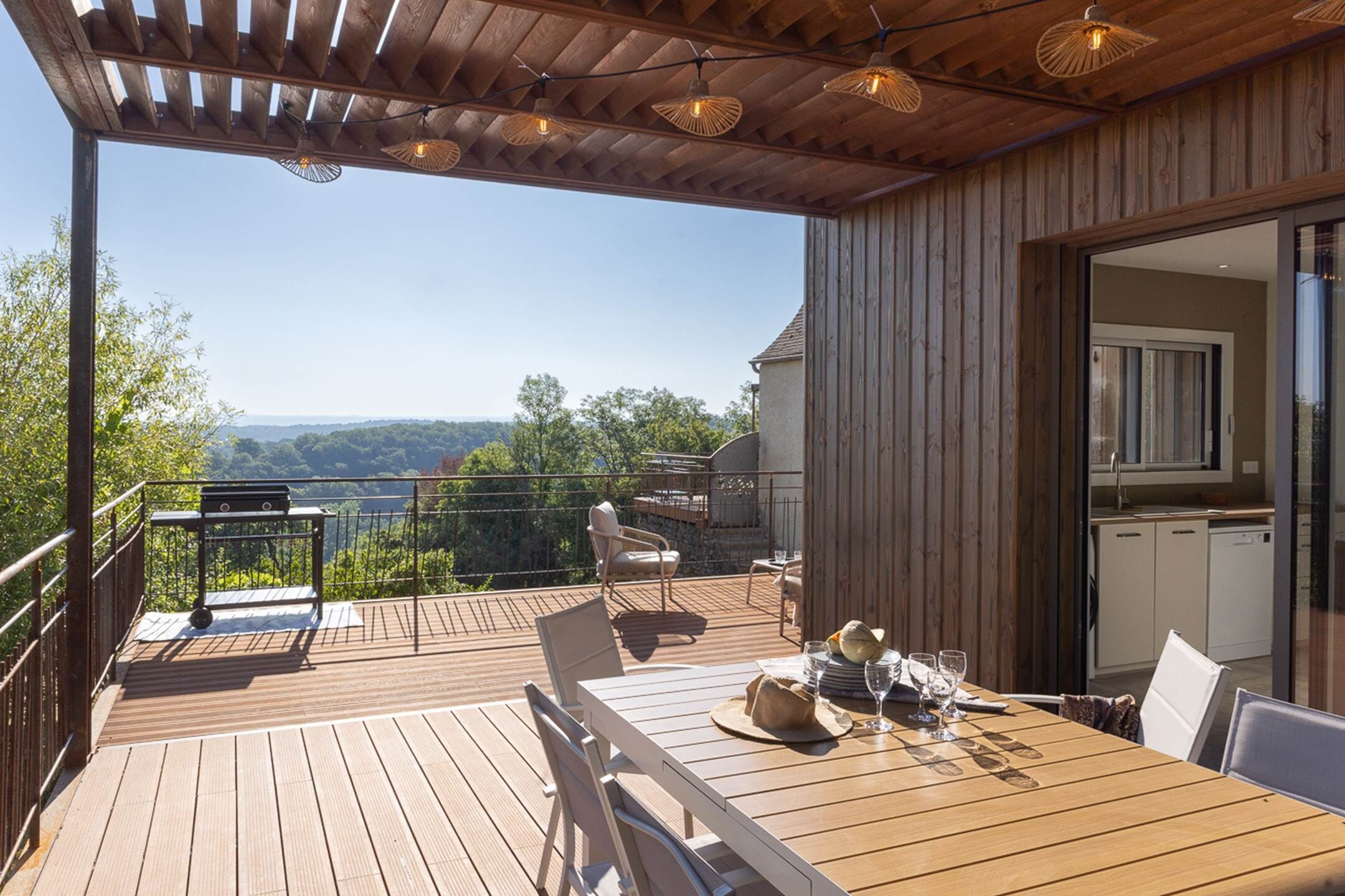 A wooden deck with a table set for dining, overlooking a scenic landscape.