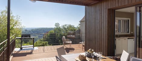 A wooden deck with a table set for dining, overlooking a scenic landscape.