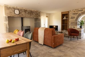 A cozy living room with a stone fireplace, a dining table with fruits, and a comfortable seating area. - In the Shadow of First Names - André's Guesthouse (Miers)