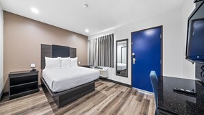 Une chambre d’hôtel comprenant un lit, une table de chevet, une télévision et un bureau avec une chaise.