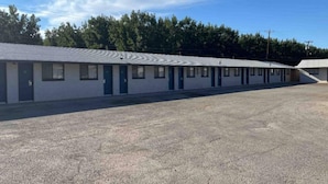 Un motel con una hilera de habitaciones, un estacionamiento y un edificio de techo plano.