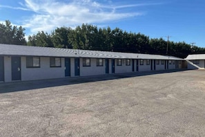 Un motel con una hilera de habitaciones, un estacionamiento y un edificio de techo plano.