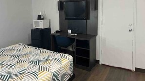 Ein Zimmer mit einem Bett, einem Schreibtisch, einem Fernseher, einer Mikrowelle und einem Sessel.