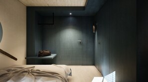 A bedroom with a bed, a bedside table, a wall-mounted shelf with a bag, and a door with a handle. - Schiffli (Rapperswil-Jona)