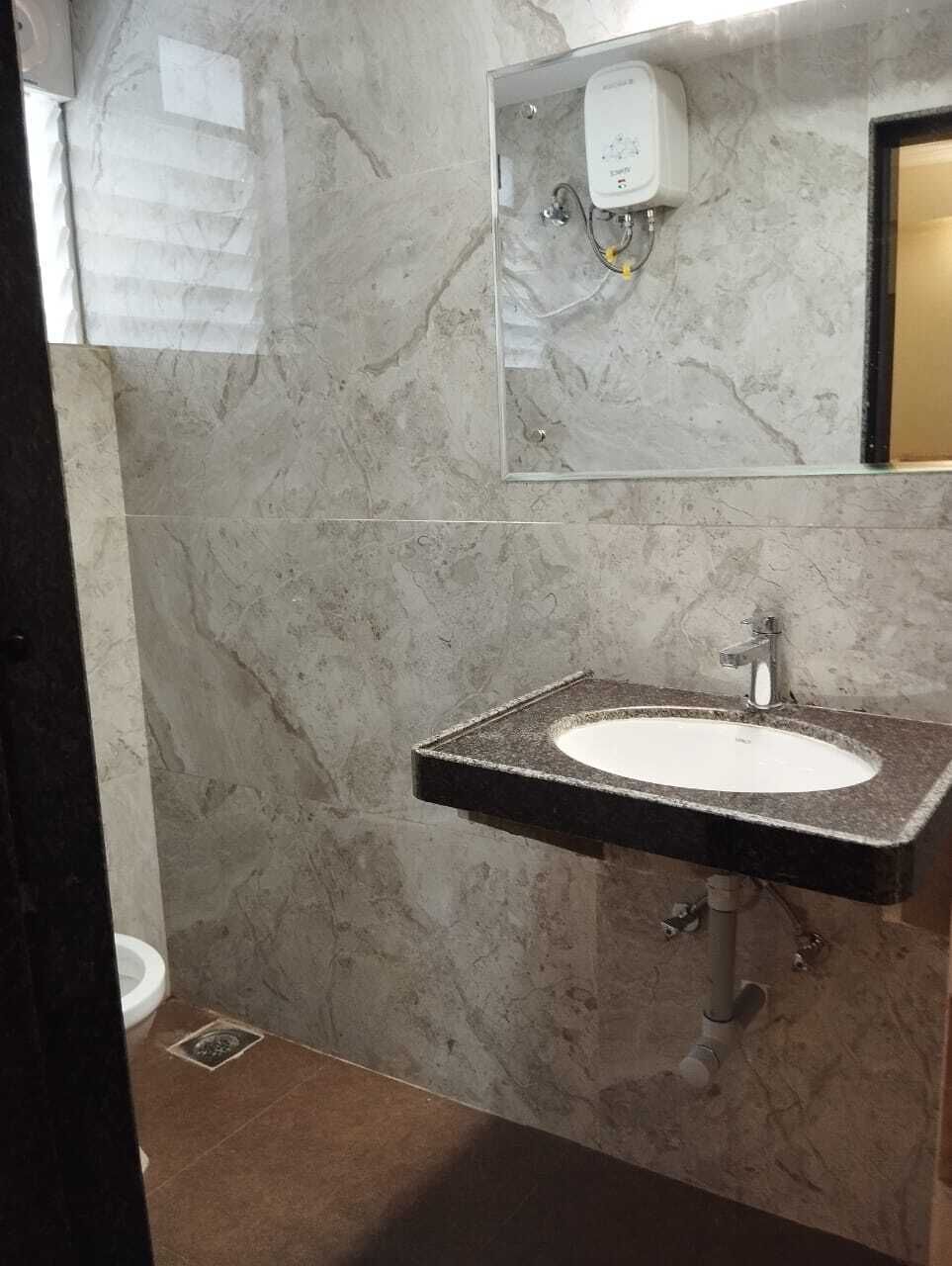 A bathroom with a marble wall, a sink with a faucet, and a soap dispenser.