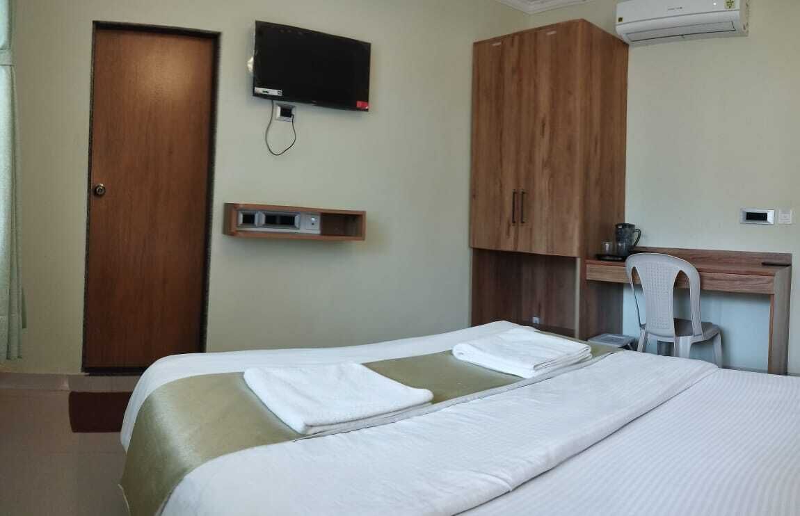 A hotel room with two beds, a TV, a desk with a chair, and an air conditioner.