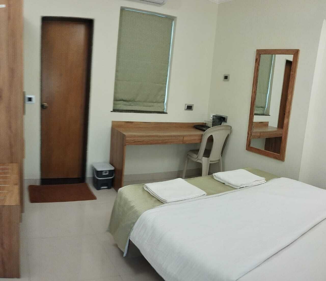 Une chambre d’hôtel équipée d’un lit, d’un bureau, d’une chaise, d’un miroir, d’une porte et d’une poubelle.