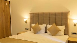 Hotellihuone, jossa on suuri sänky, kaksi yöpöytää, puuovi ja seinään kiinnitetyt valaisimet.