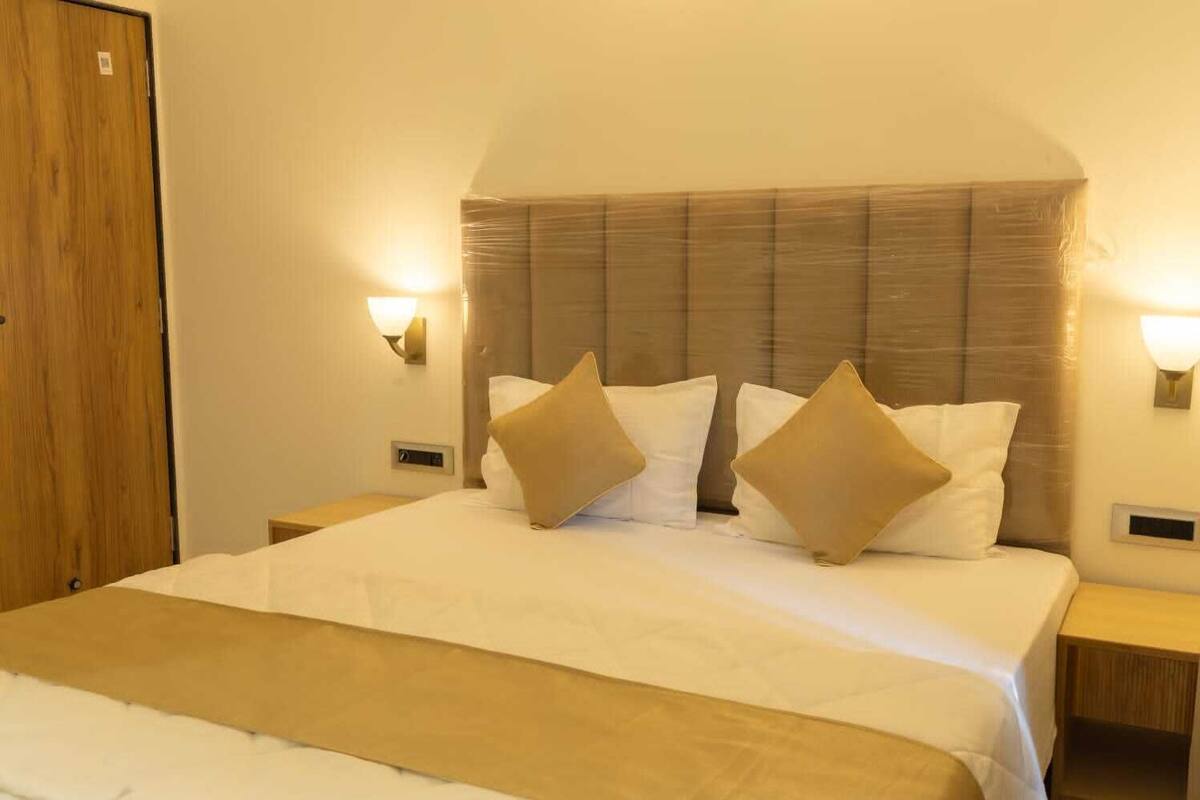 A hotel room with a large bed, two bedside tables, a wooden door, and wall-mounted lights.
