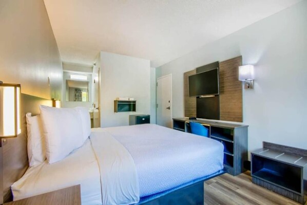 Una habitación de hotel con una cama, un escritorio, una silla, un televisor y un televisor montado en la pared.