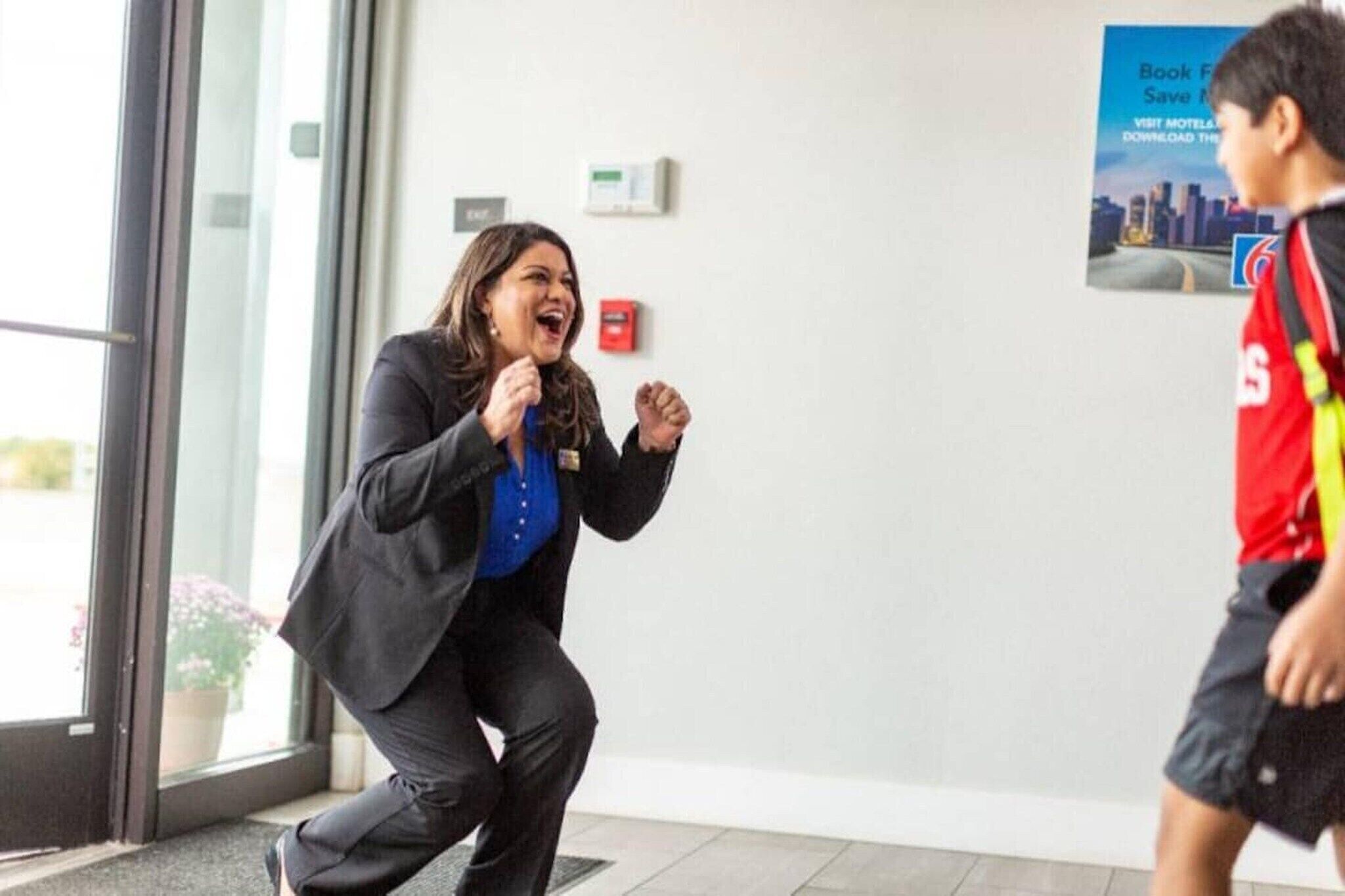 A person crouching in a doorway, a fire alarm on the wall, and a poster advertising a hotel.