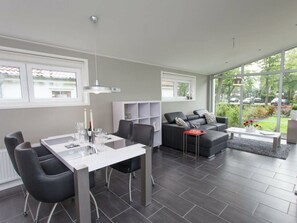 A modern living room with a dining area, grey sofas, a coffee table, and large windows offering a view of the outside. - Holiday Home in Dordrecht With Terrace (Dordrecht)