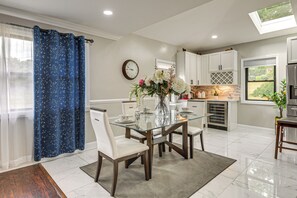 A modern kitchen with white cabinets, a glass dining table, and a decorative vase with flowers.
