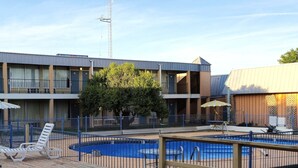 A hotel with a pool, lounge chairs, and a fenced deck area.