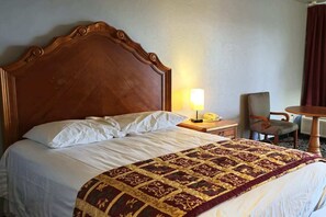 Une chambre d’hôtel avec une tête de lit en bois, un lit recouvert de draps blancs, un plaid à motifs, une lampe de chevet, une chaise et une petite table avec un téléphone.