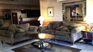 A hotel lobby with two patterned sofas, a round coffee table, a lamp, a mirror, and a small table with a lamp.