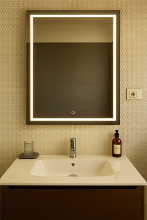 Un baño con un espejo grande, un lavabo, un grifo, dispensador de jabón e interruptor de luz.