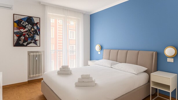 A bedroom with a bed, bedside tables, a radiator, a window, and a wall art piece.