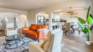 Een moderne woonkamer met een bank, fauteuil, salontafel, en een eethoek met stoelen en een tafel.