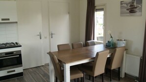 A dining area with a wooden table and chairs, a kitchen with a stove and oven, a clock on the wall, and a window with curtains. - Holiday Home in Dordrecht With Terrace (Dordrecht)