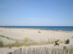 A beach with a wooden fence, a yellow scooter, and a few people.