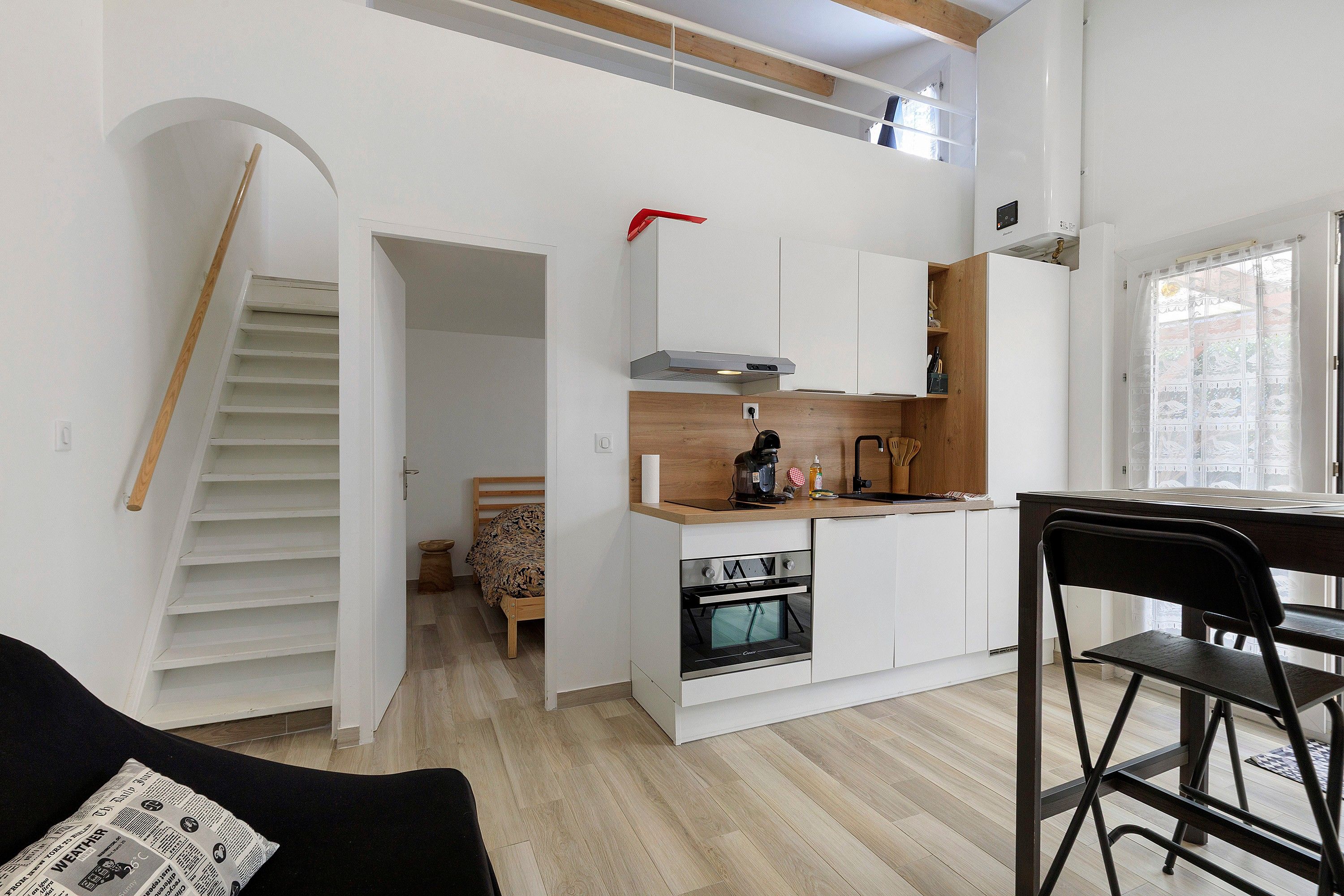 Un ambiente living compatto con angolo cottura, zona pranzo e una scala che conduce a un piano superiore.