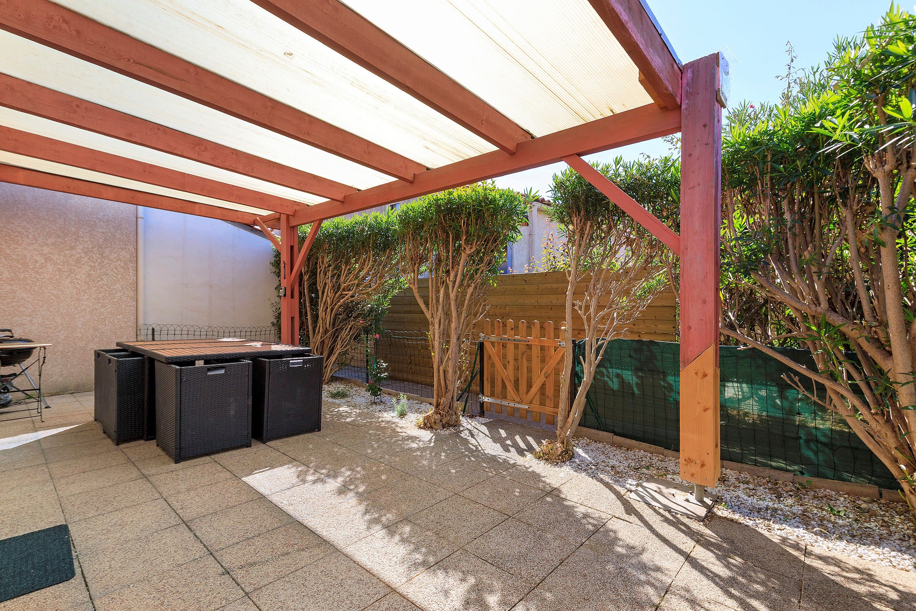 Un patio exterior con zona de estar techada, una parrilla y una valla de madera.