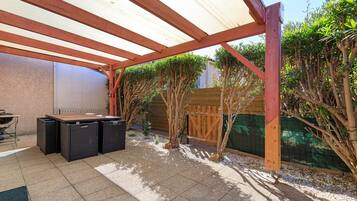 Un patio exterior con zona de estar techada, una parrilla y una valla de madera.